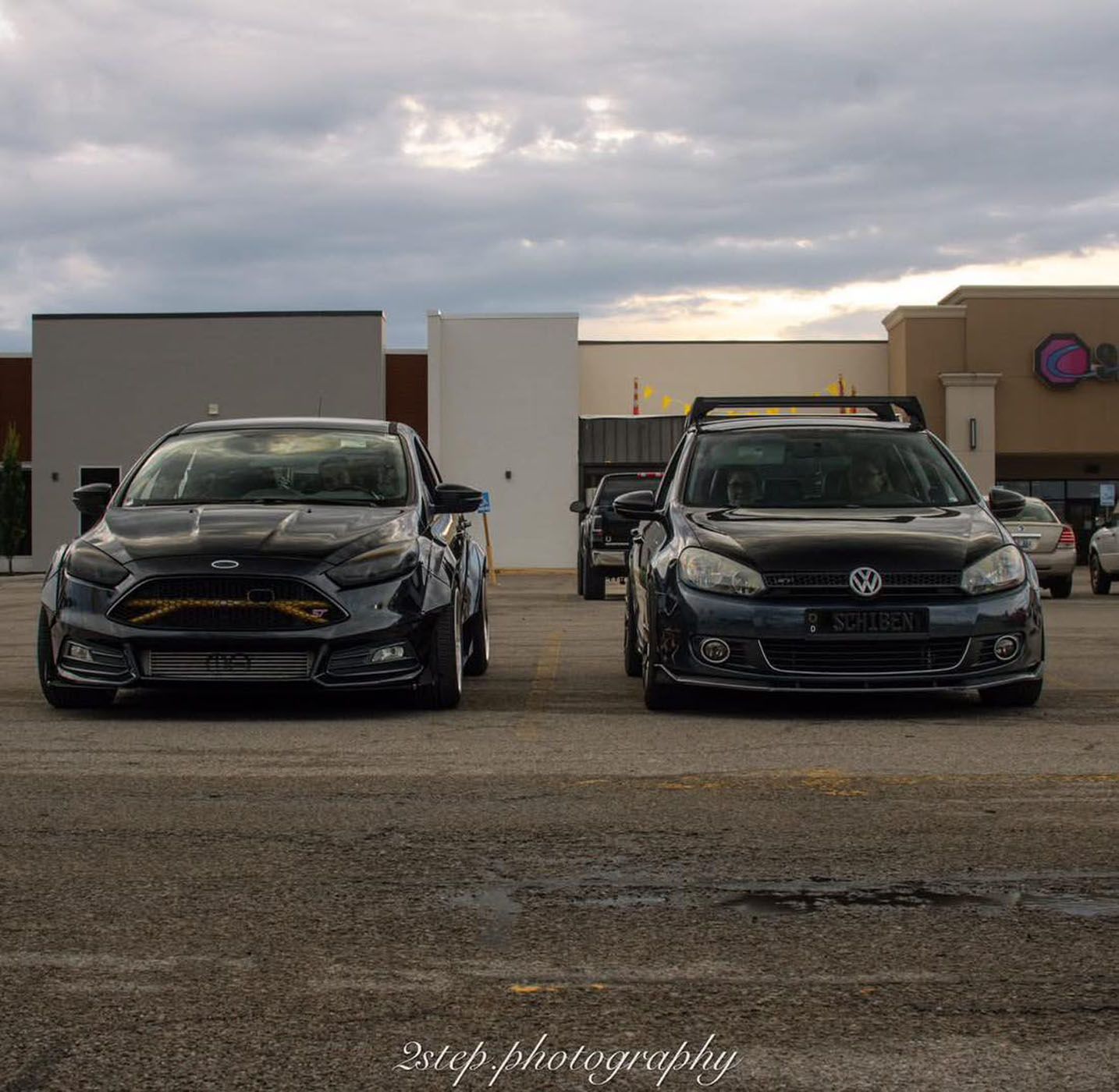 Two black sports cars parked side by side in front of a building at dusk