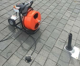 Orange cable reel machine on a paved sidewalk beside a small pole and loose cable