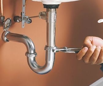 Hand tightening a wrench on a chrome sink trap under a bathroom sink
