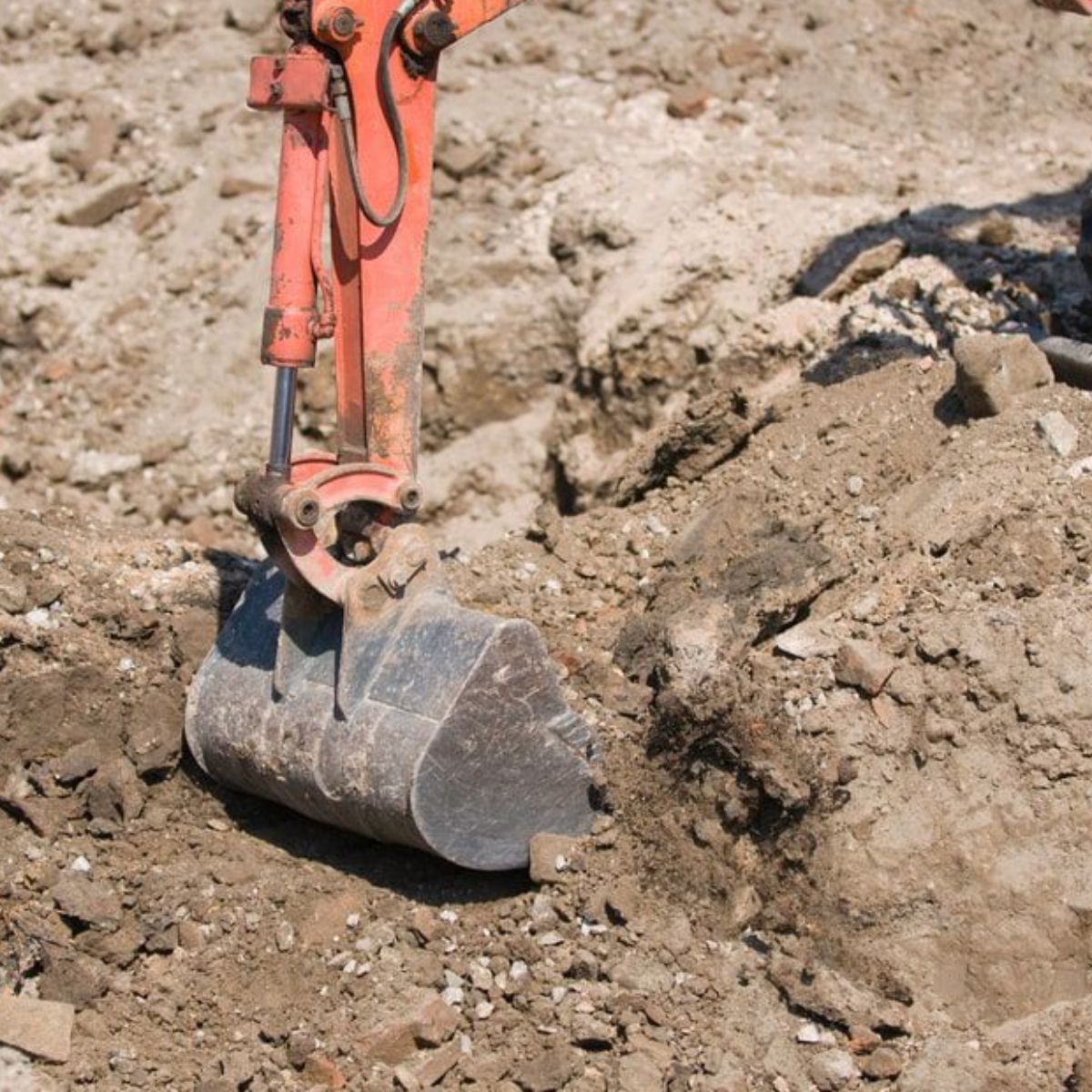 An orange excavator is digging a hole in the dirt