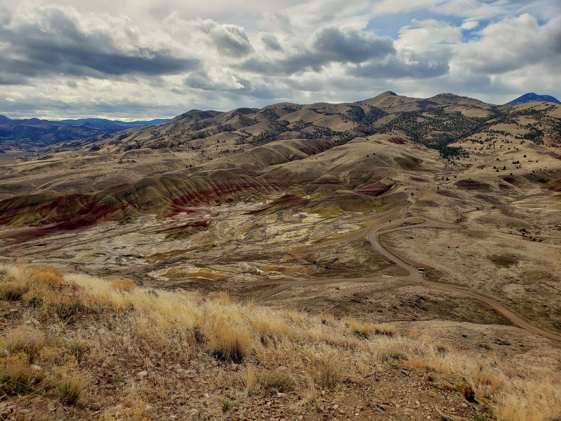 Rolling hills and mountains under a cloudy sky. The landscape features shades of brown and red.