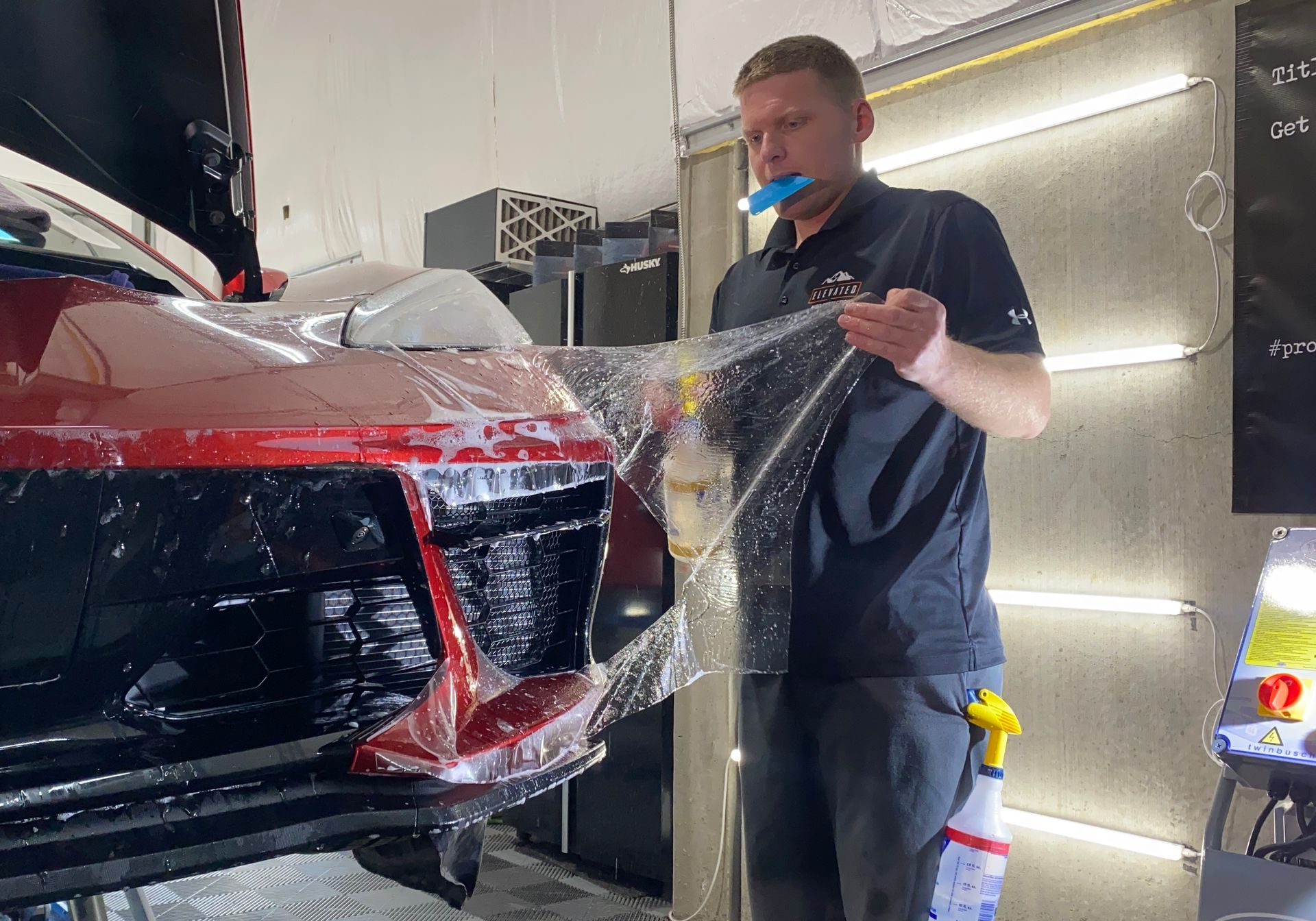 A man is covering the front of a car with plastic wrap.