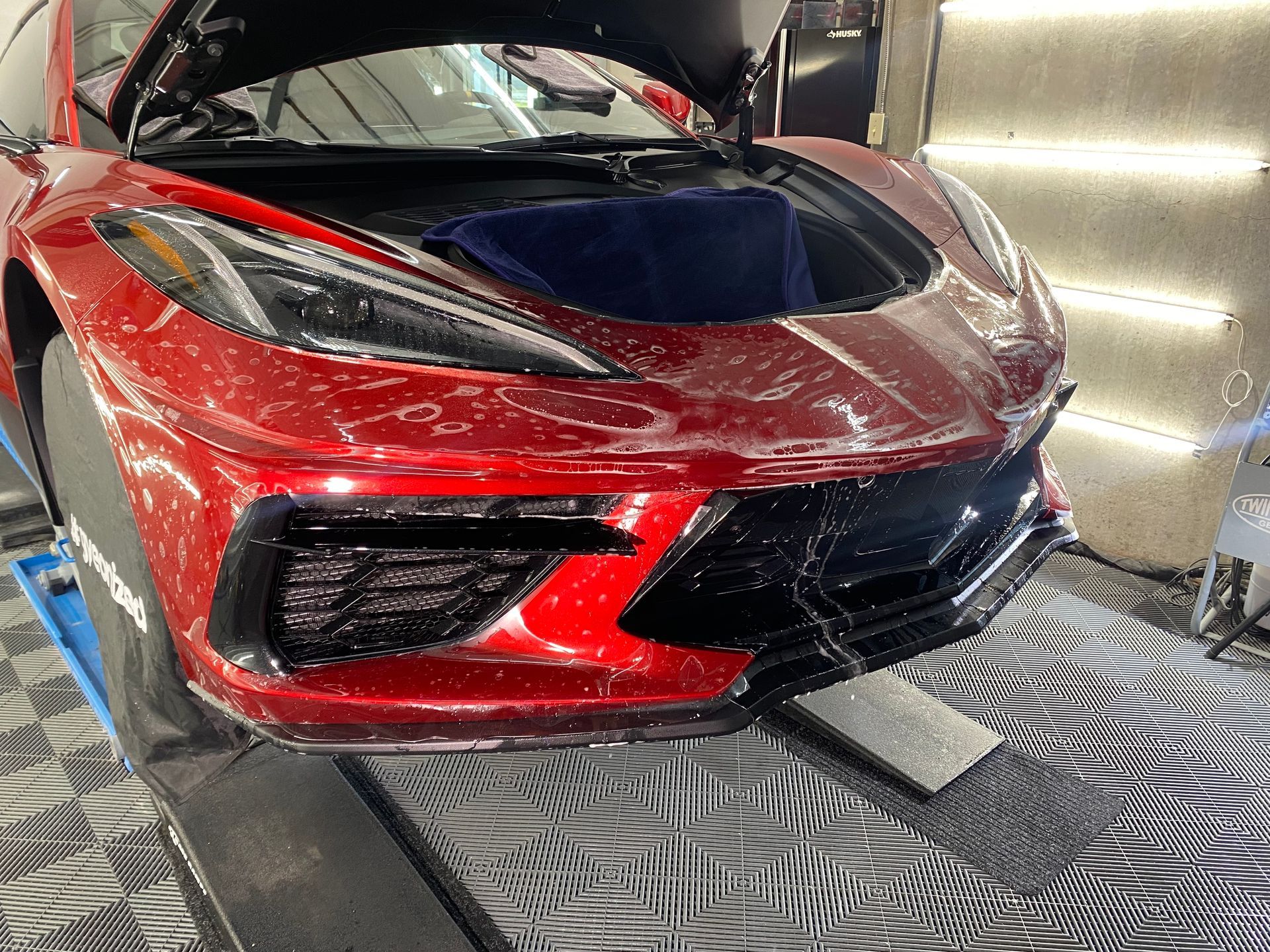 A red sports car with the hood open is sitting on a tiled floor.