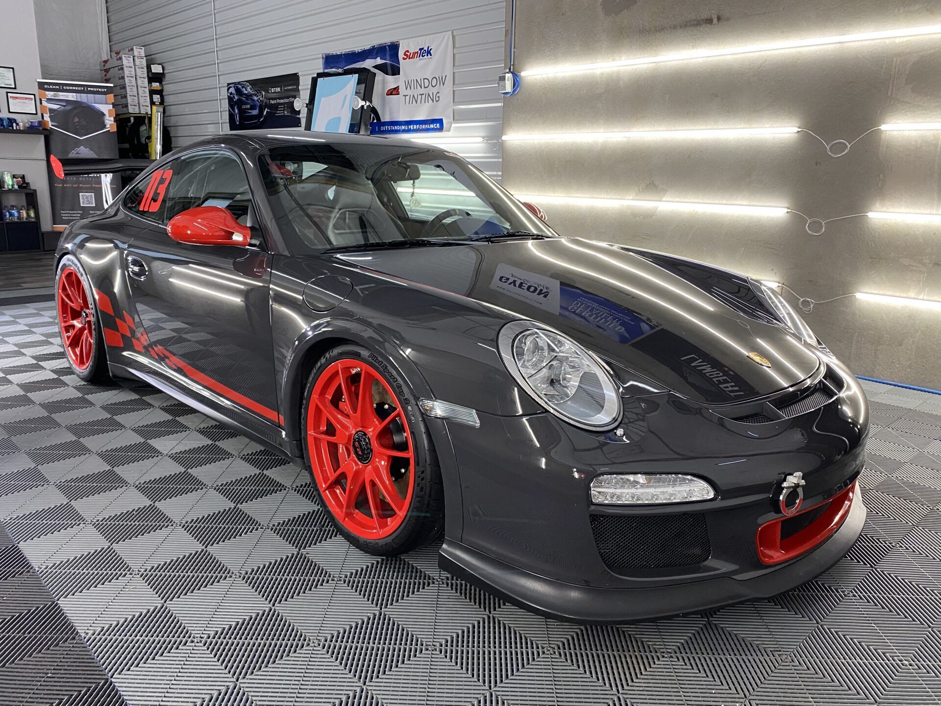 A gray porsche 911 gt3 rs with red wheels is parked in a garage.