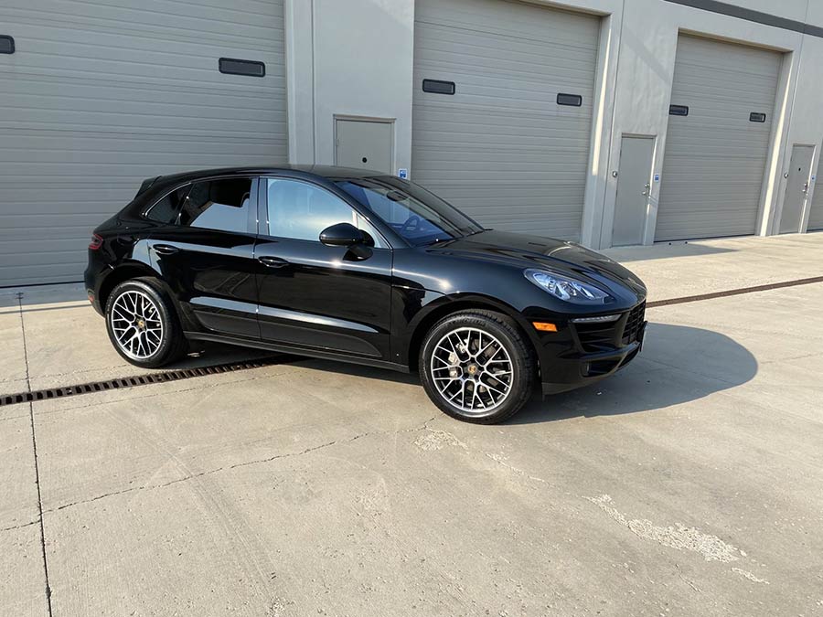 A black porsche macan is parked in front of a garage.