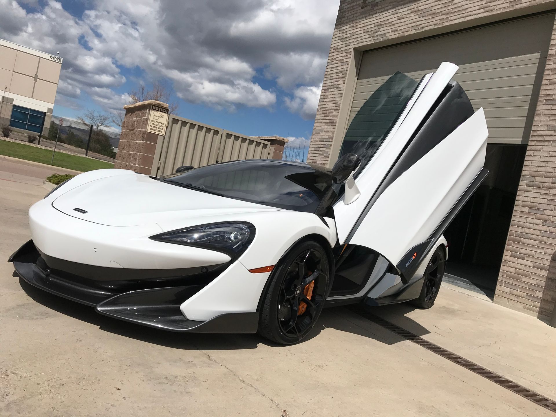 A white sports car with its doors open is parked in front of a garage.