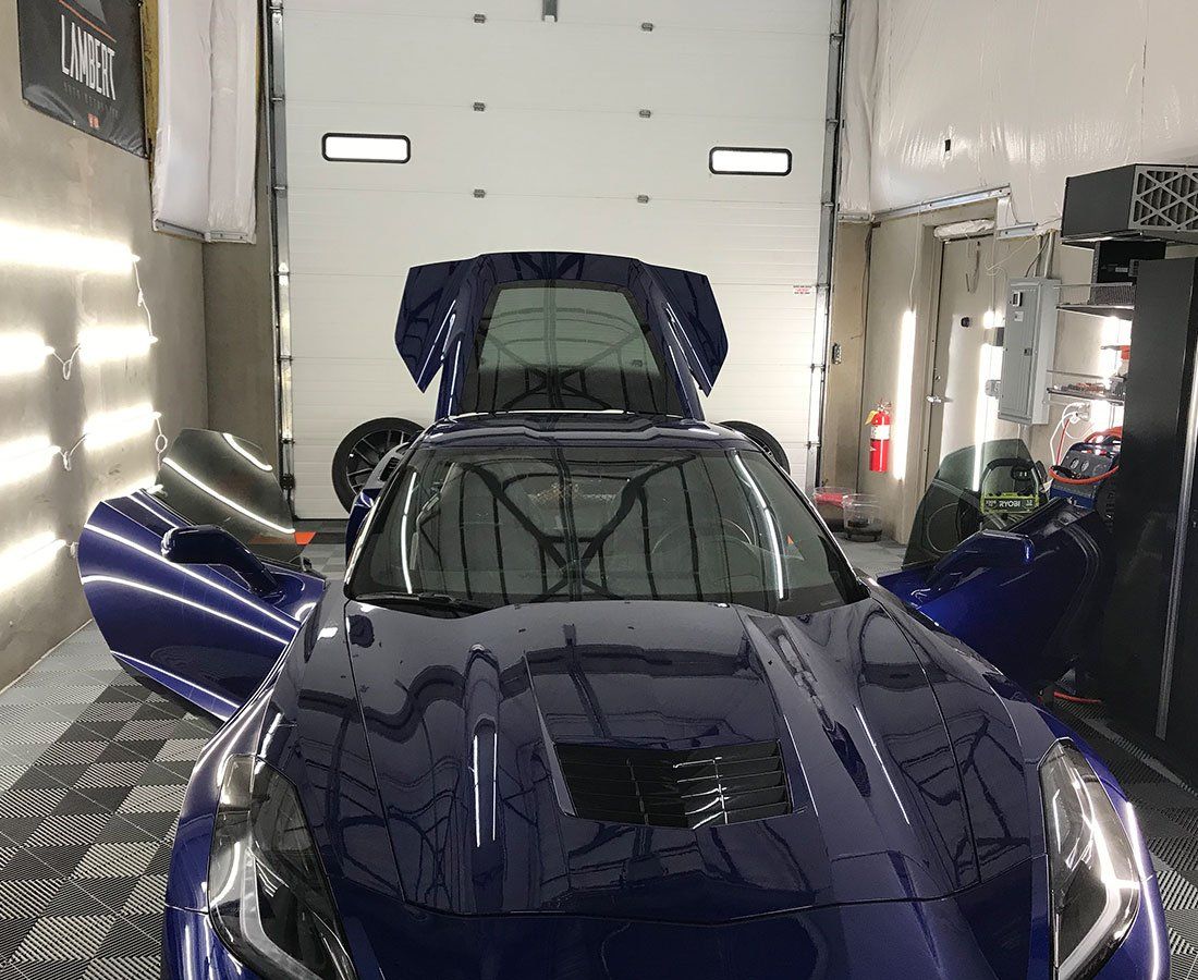A blue sports car with the hood up is parked in a garage.