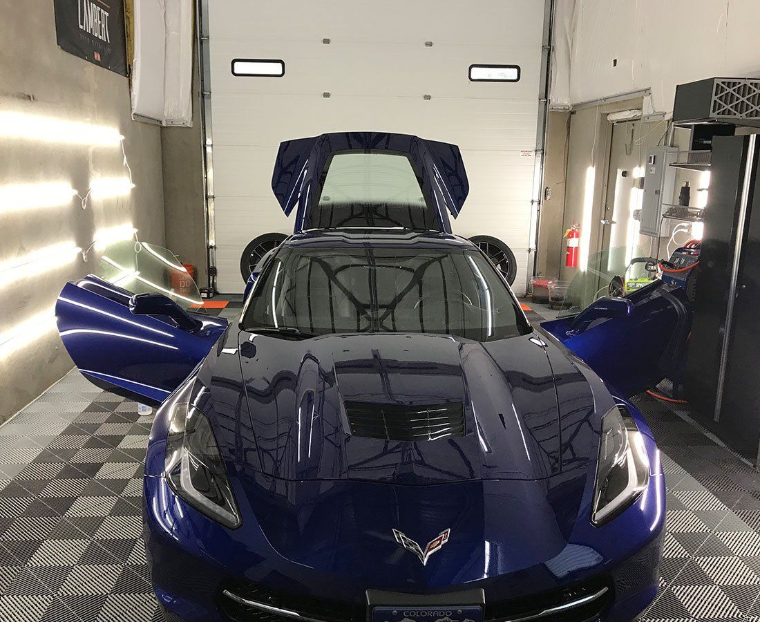 A blue sports car is parked in a garage with its doors open.