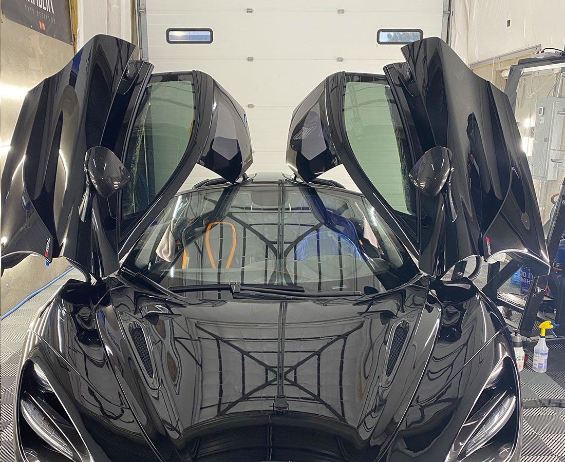 A black sports car with its doors open is parked in a garage.