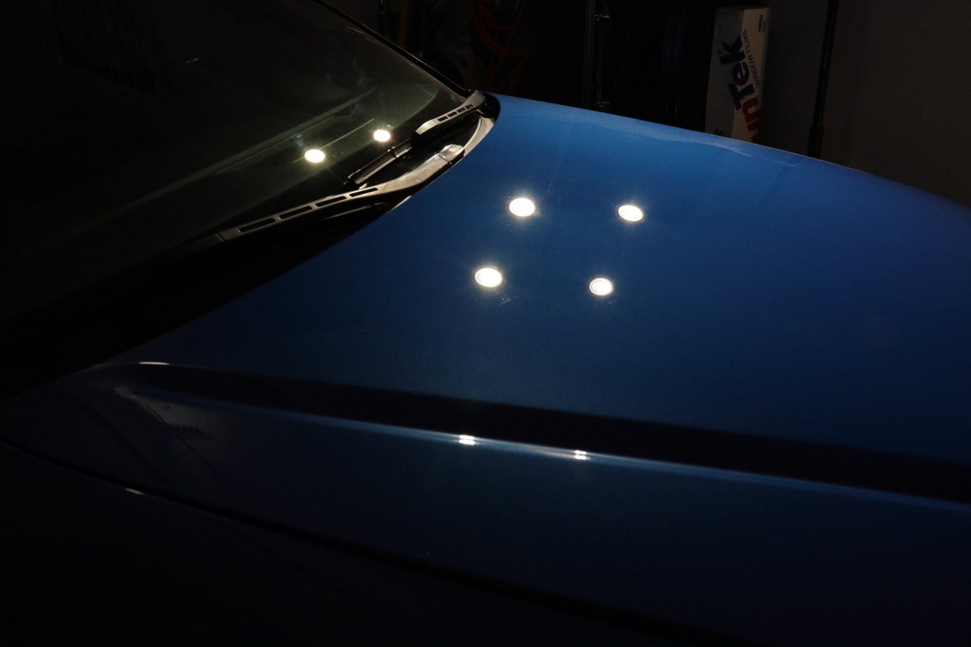 The hood of a blue car is lit up at night