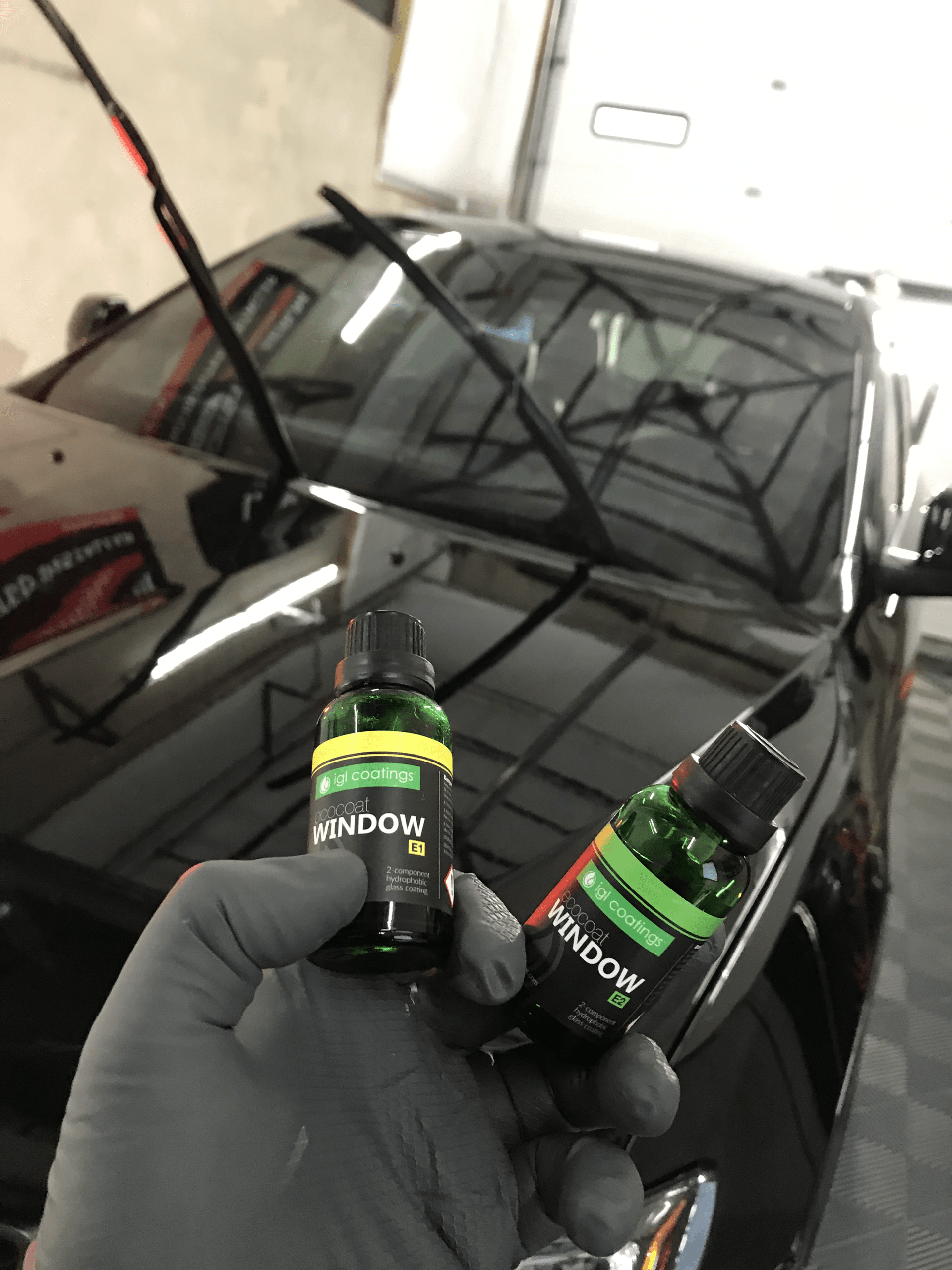 A person is holding two bottles of window cleaner in front of a car