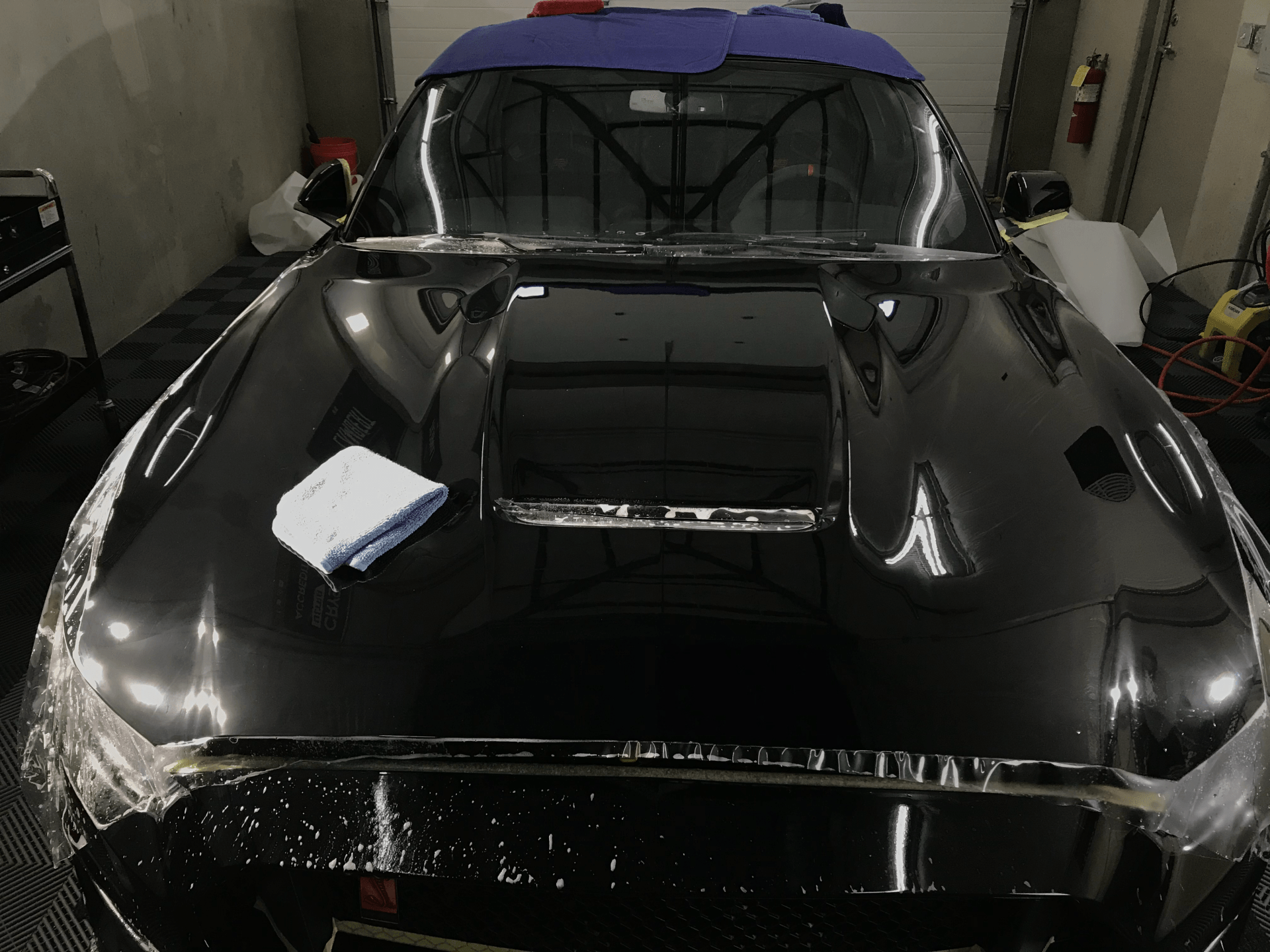 A black car is wrapped in plastic in a garage