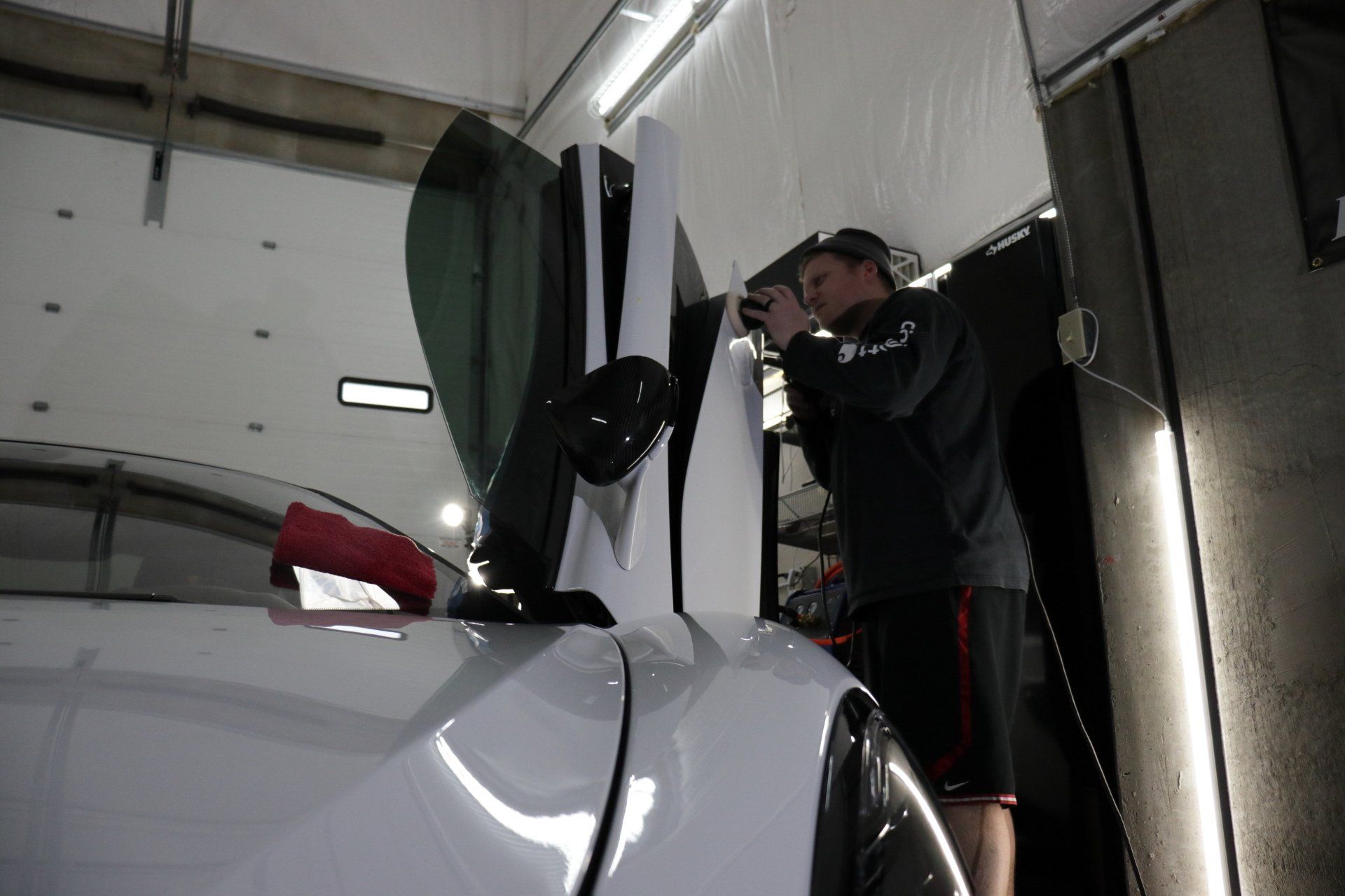 A man is standing next to a white car in a garage.