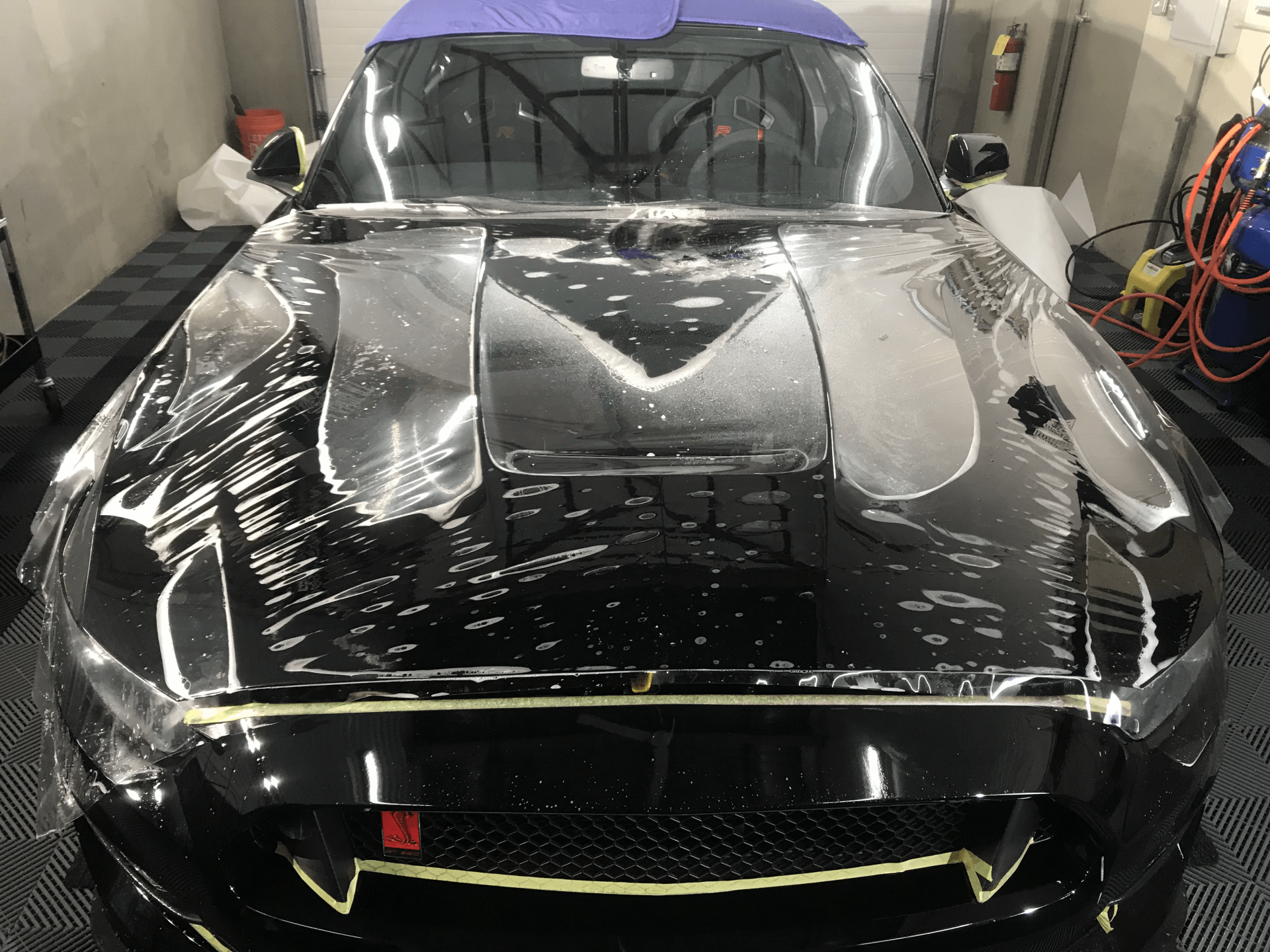 A black car is wrapped in plastic in a garage.