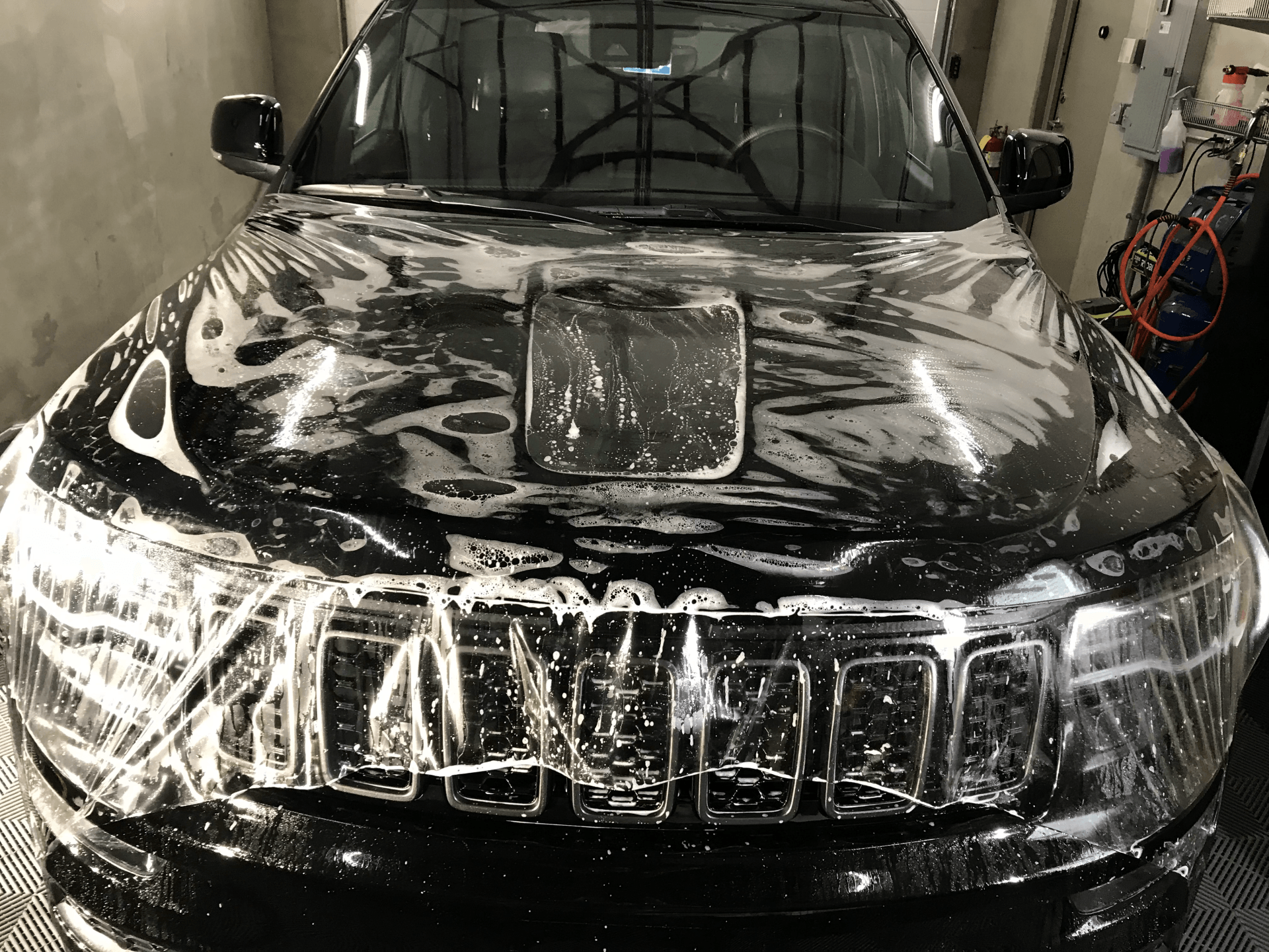 A black car is covered in soap and water in a garage.