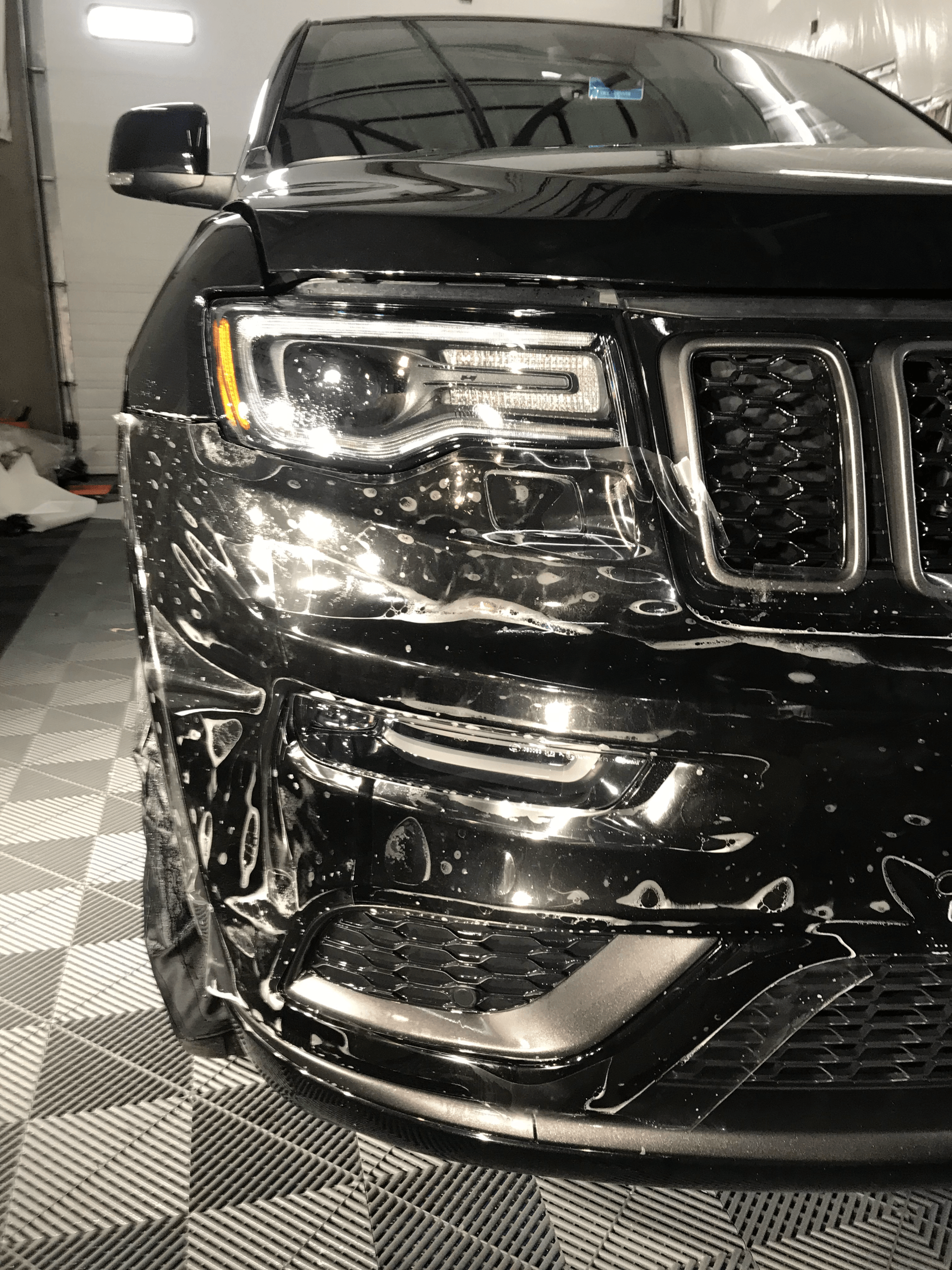 A black jeep grand cherokee is covered in plastic wrap in a garage.