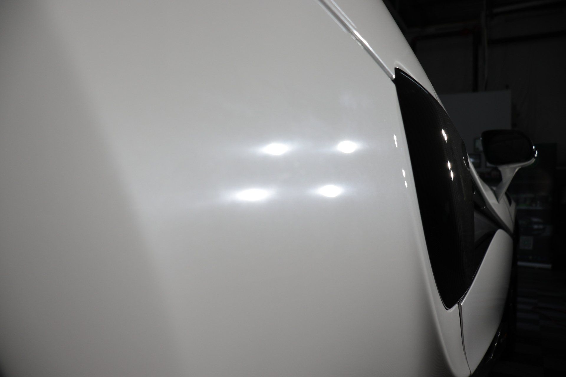 A white car is parked in a dark room in a garage.