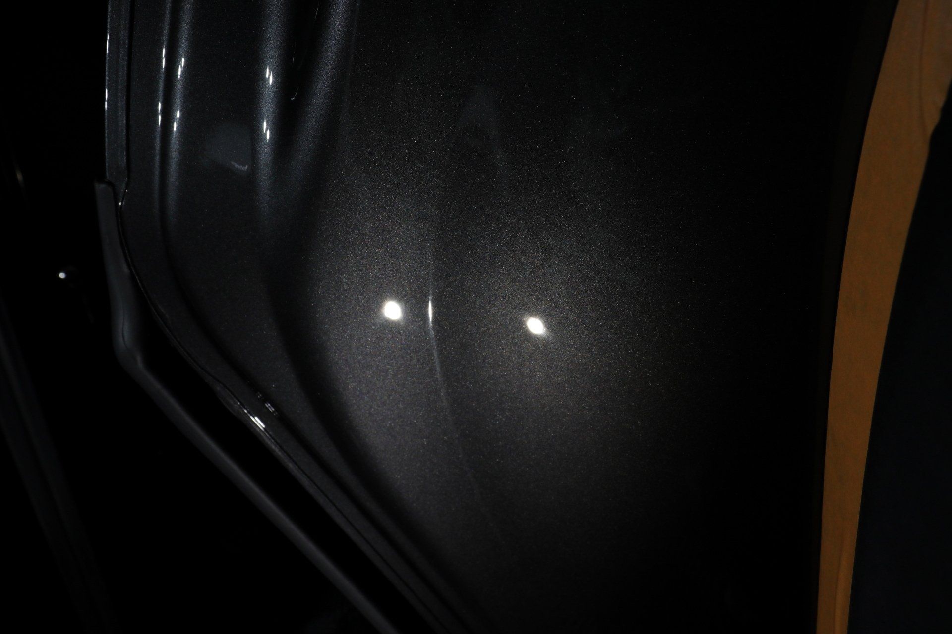 A close up of a black car door with a few white spots on it.