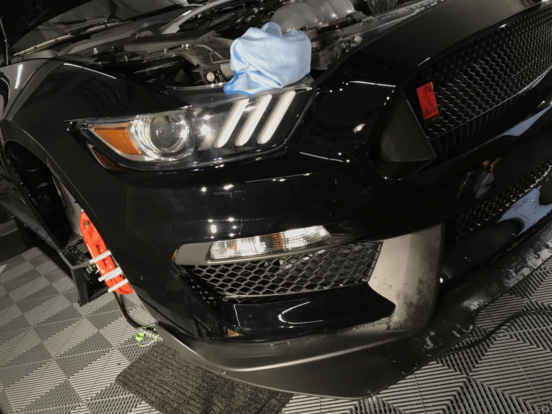 A black ford mustang with the hood open is sitting on a checkered floor.
