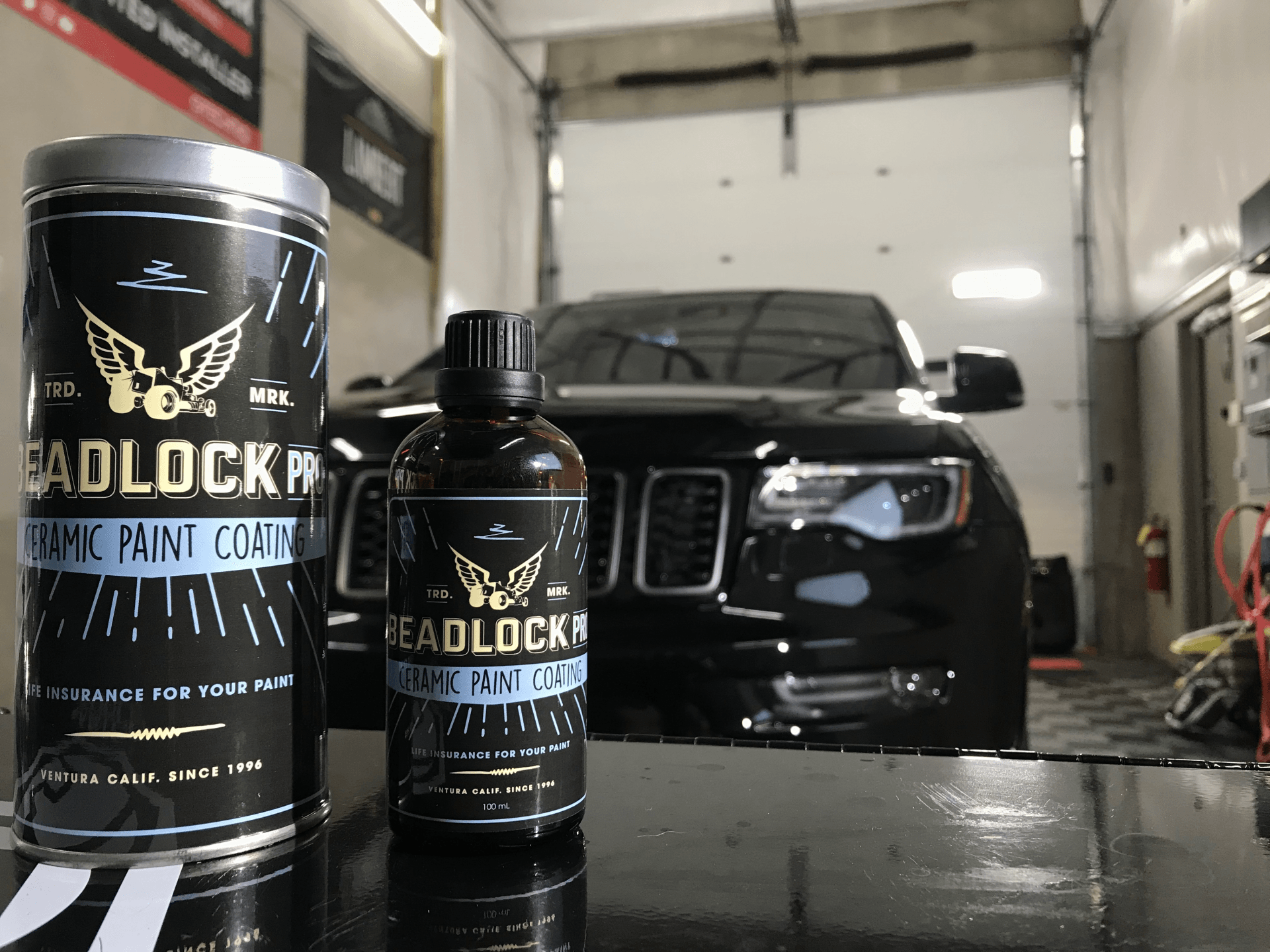 A black car is parked in a garage next to a bottle of headlock paint coating.