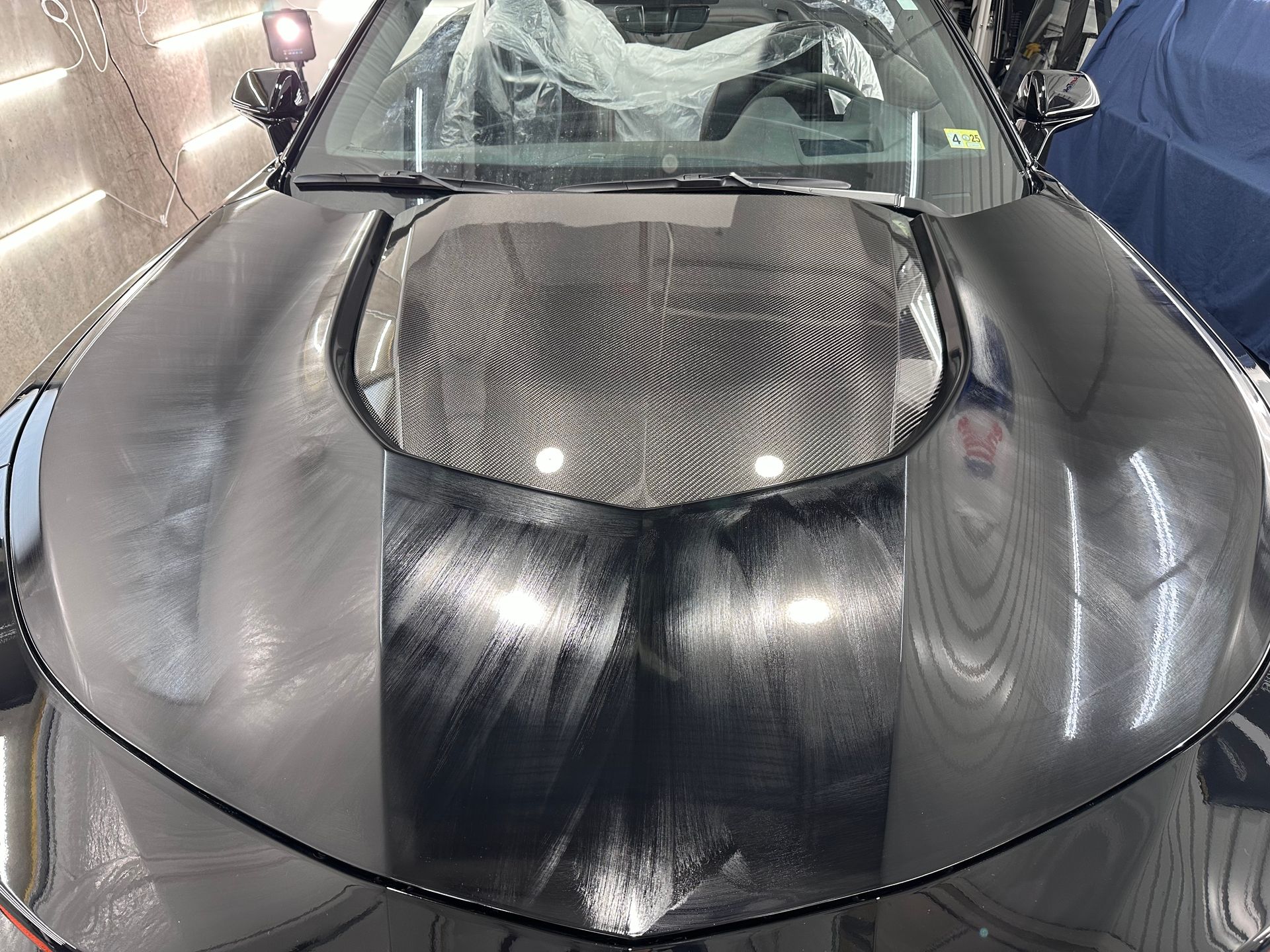 The hood of a black car is sitting in a garage.