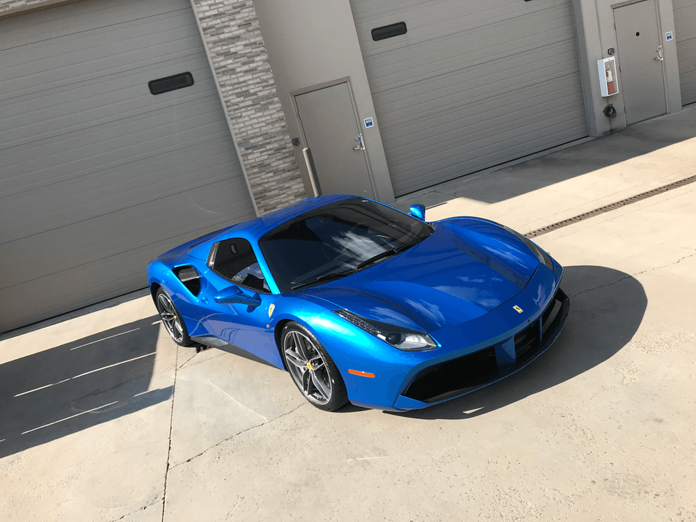A blue sports car is parked in front of a garage.
