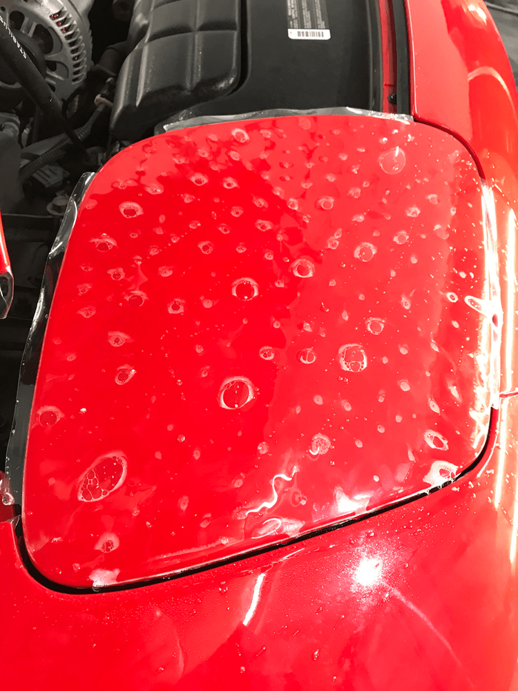 A close up of a red car with water drops on the hood.