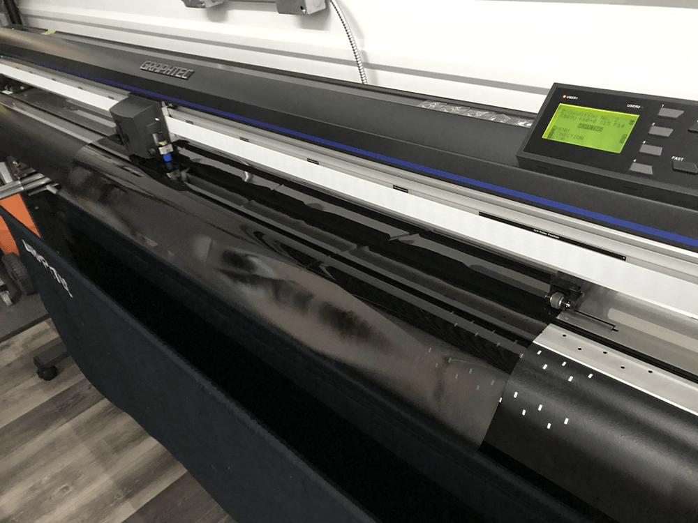 A large printer is sitting on a wooden floor in a room.