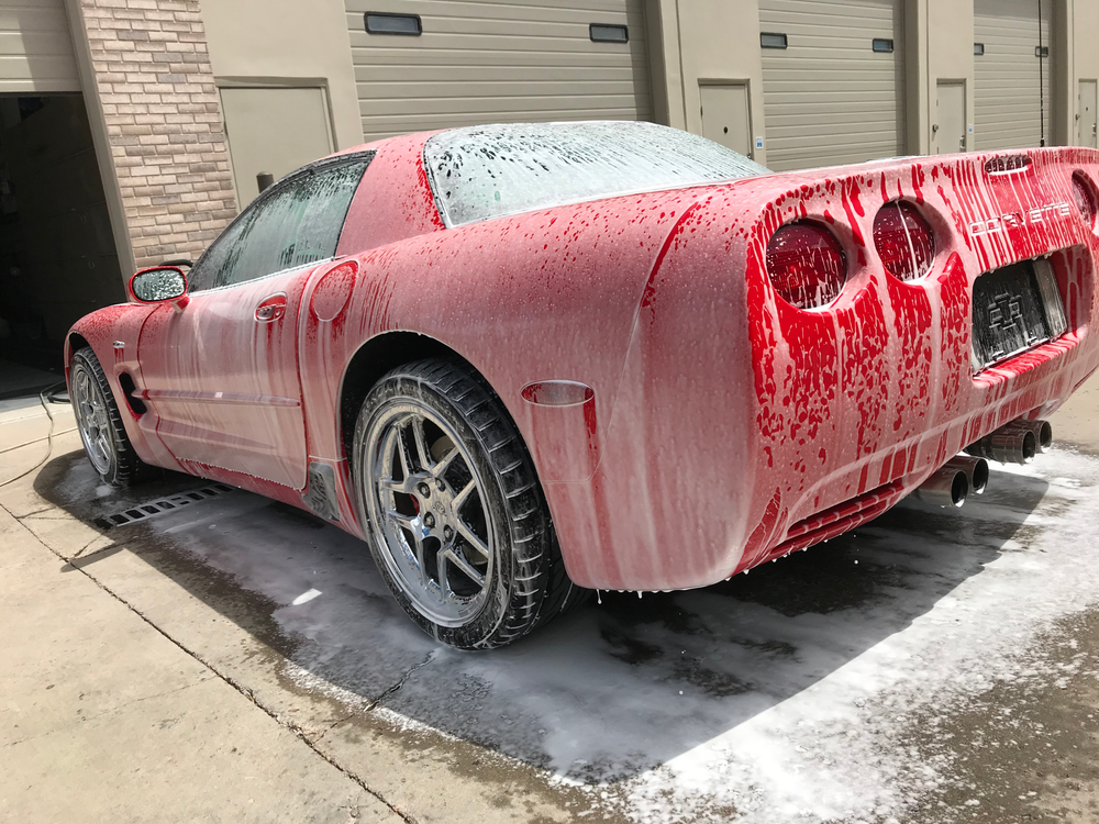 A red corvette is covered in foam in a parking lot.
