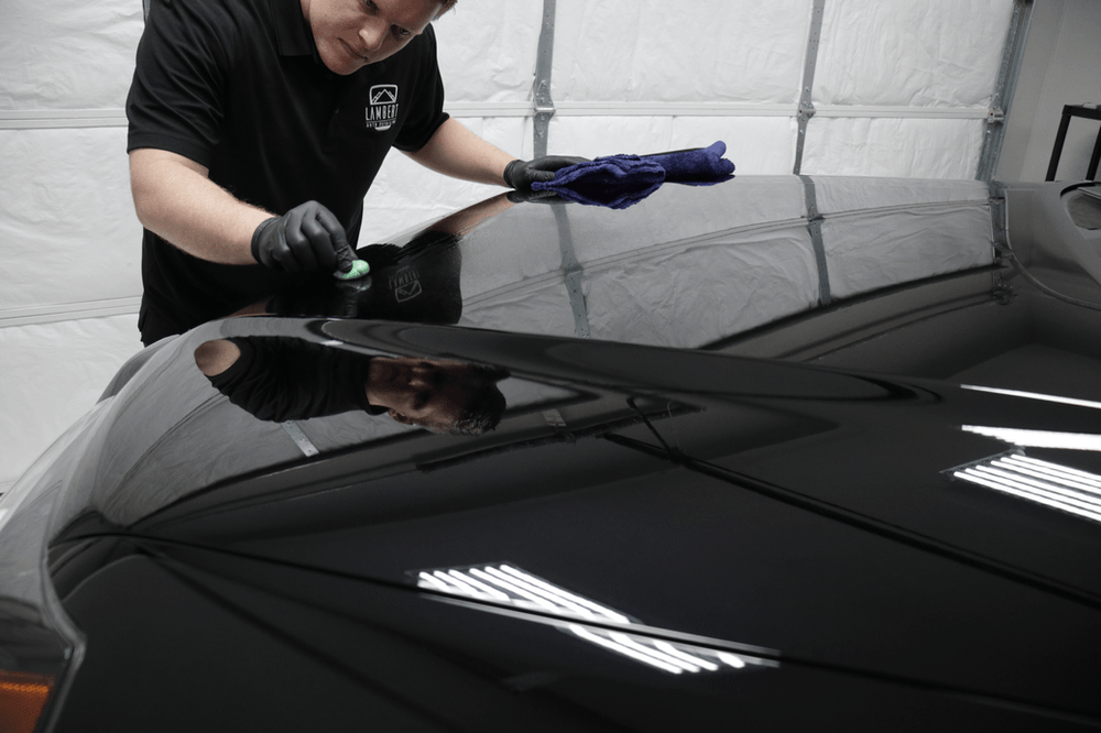 A man is polishing the hood of a black car in a garage.