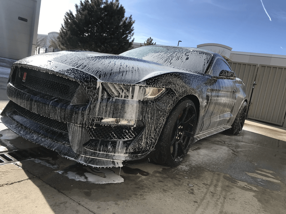 A ford mustang is covered in foam and is sitting in a parking lot.