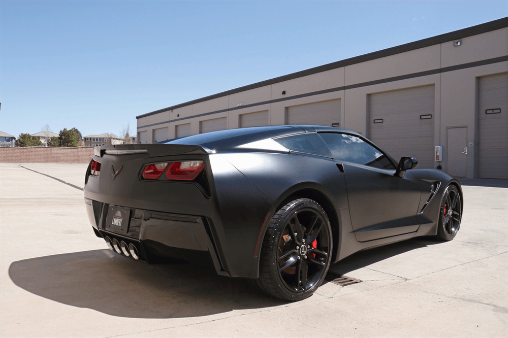 A black corvette is parked in front of a building.