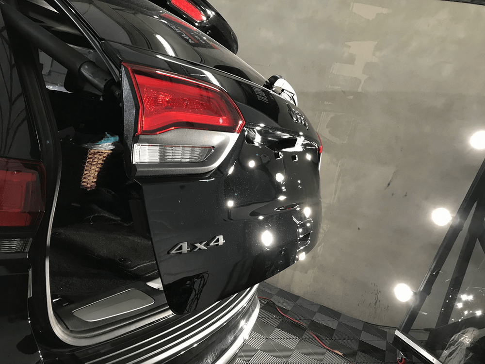 A black car with the trunk open is parked in a garage.