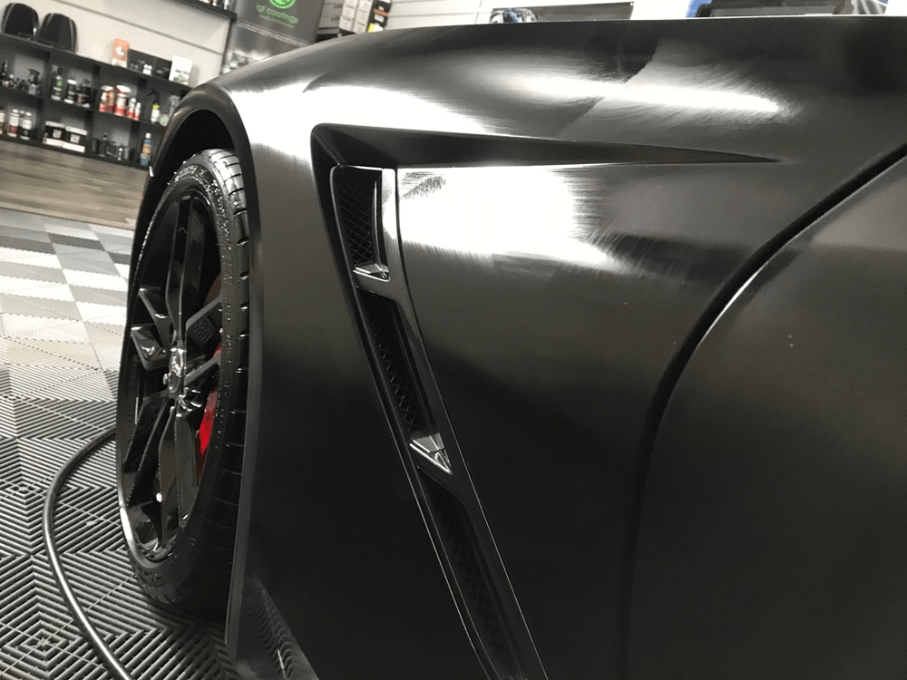 A black sports car is parked on a checkered floor in a garage.