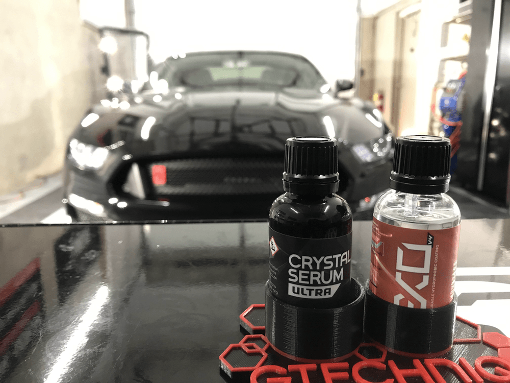 Two bottles of gtechniq crystal serum ultra are sitting on a table in front of a car.