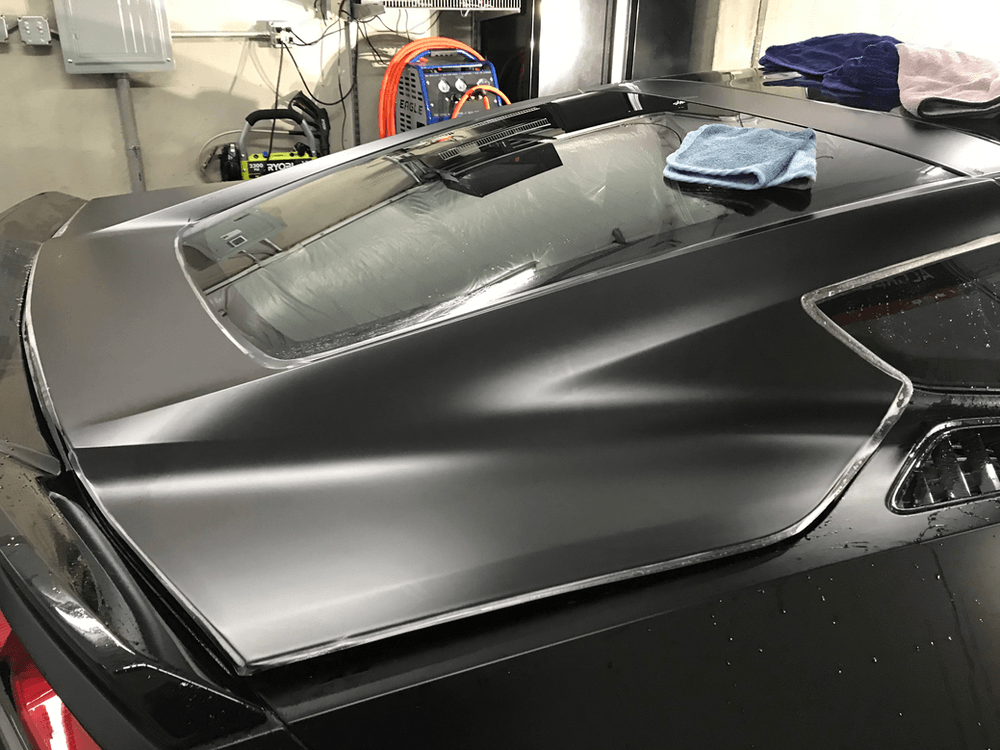 A black car is parked in a garage with a cloth on the roof.