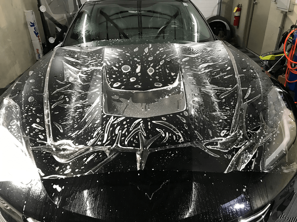 A black car is covered in plastic wrap in a garage.