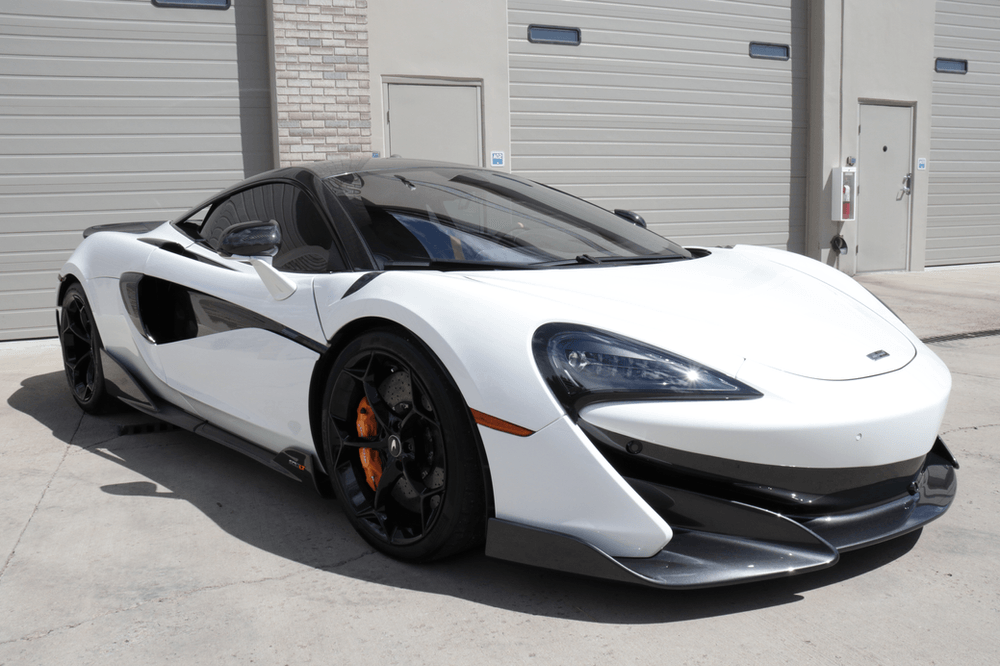 A white sports car is parked in front of a garage door.