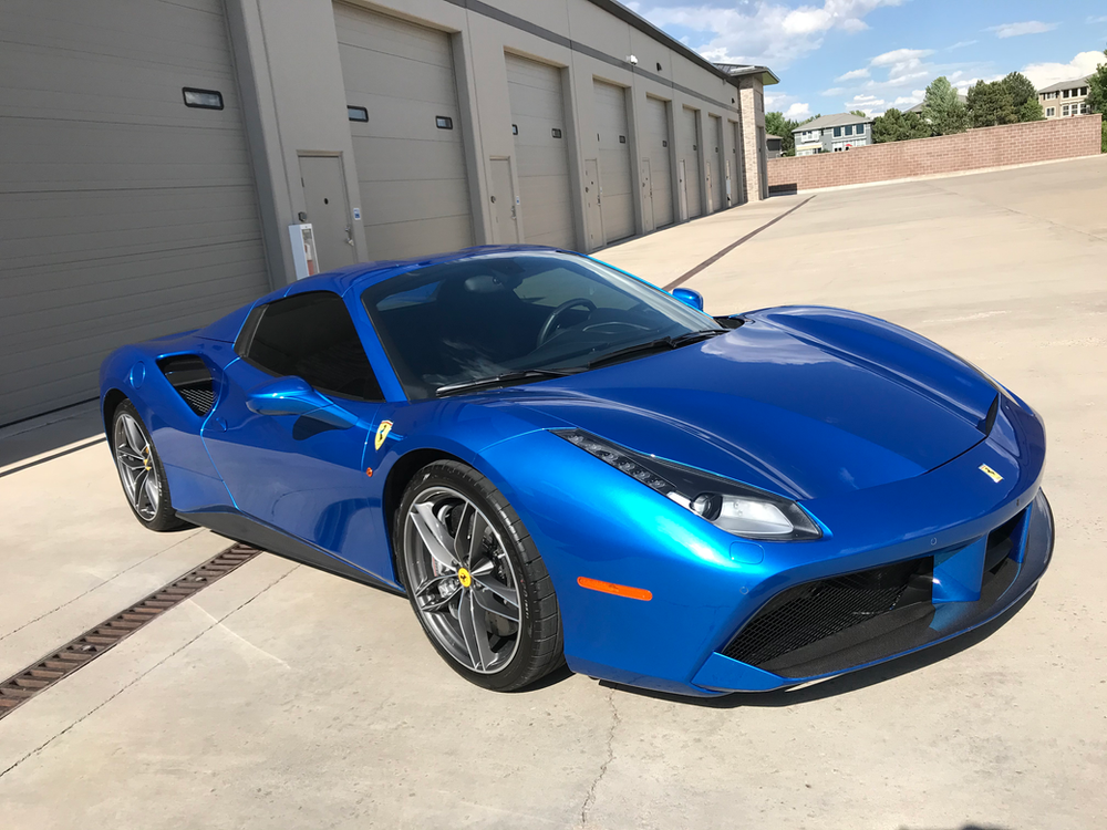 A blue ferrari 488 gtb is parked in front of a garage.