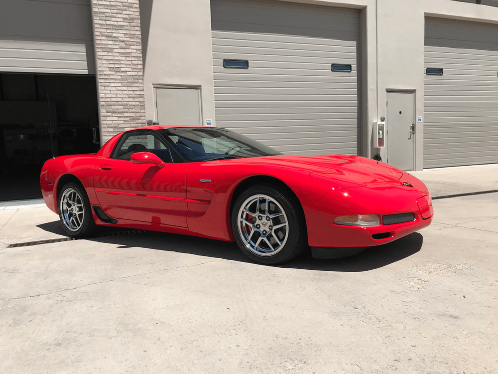 A red corvette is parked in front of a garage.