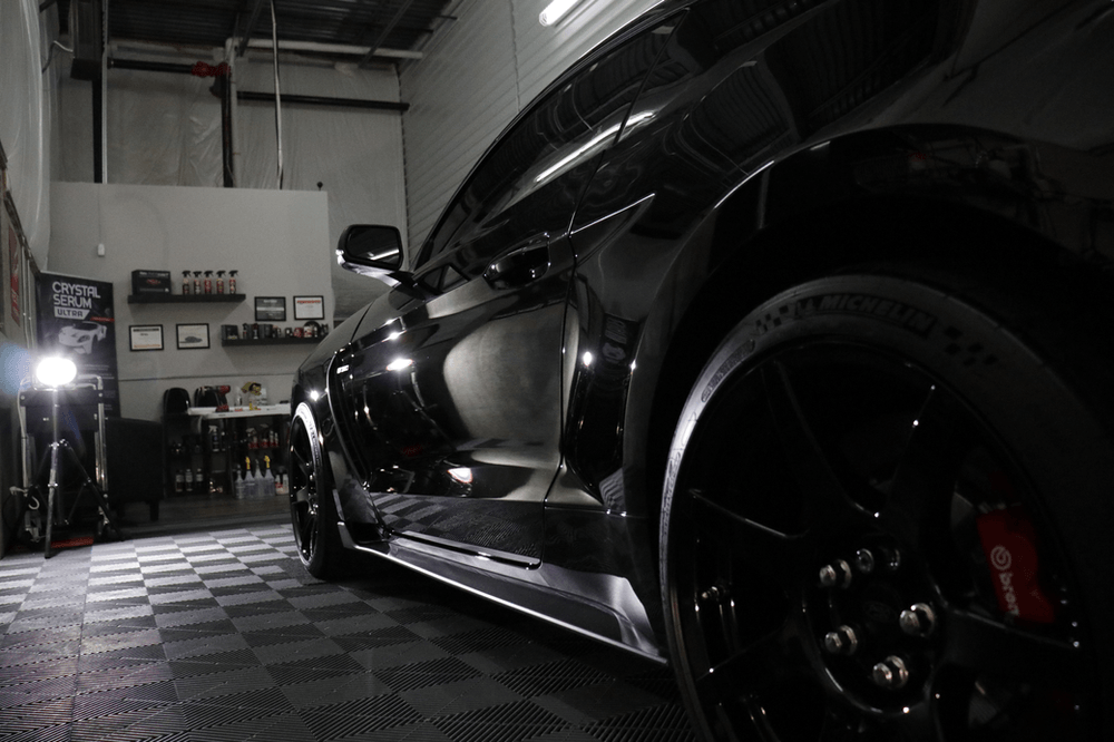 A black car is parked in a garage with a checkered floor.
