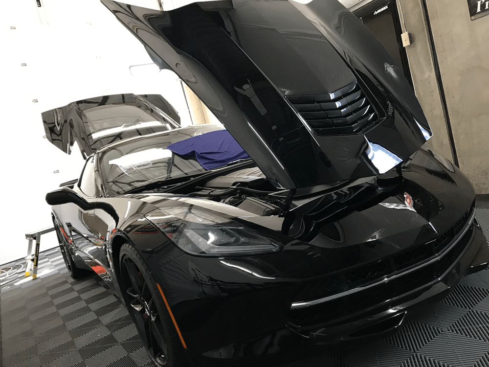 A black sports car with the hood up is parked in a garage.