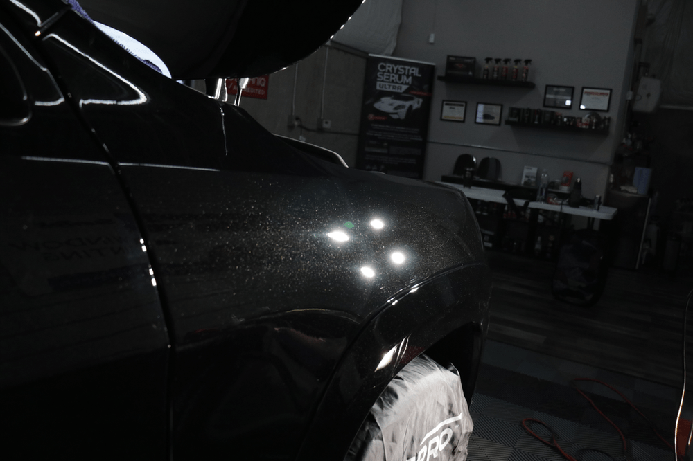 A person is standing next to a black car in a garage.