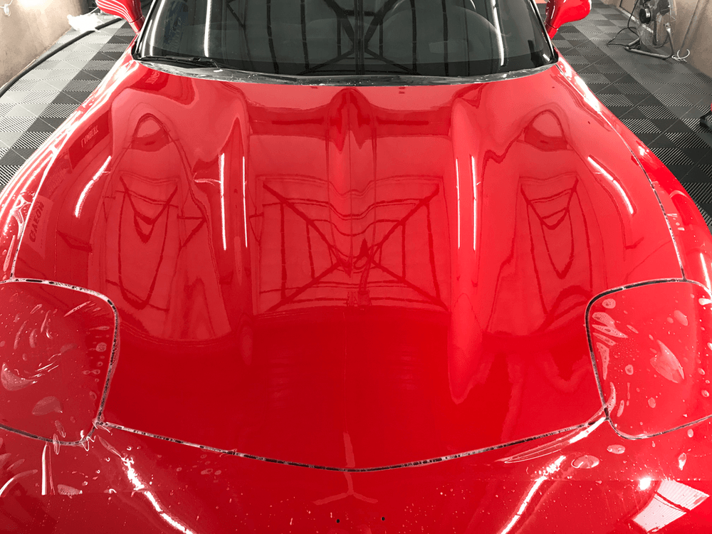 The hood of a red sports car is reflected in the windshield.