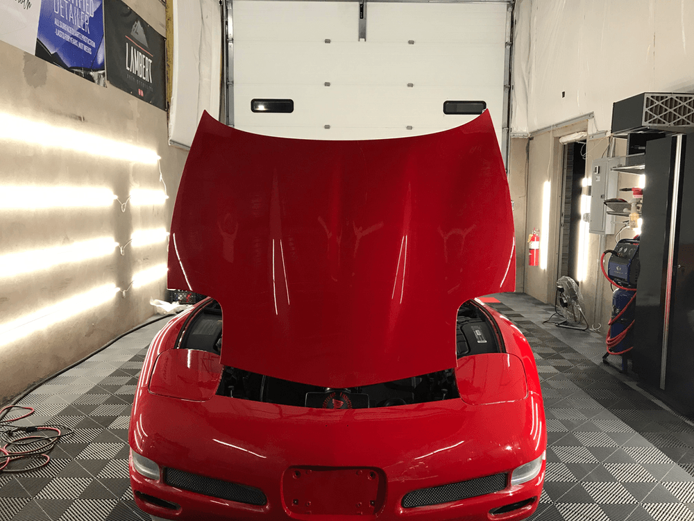 A red sports car with the hood up in a garage.