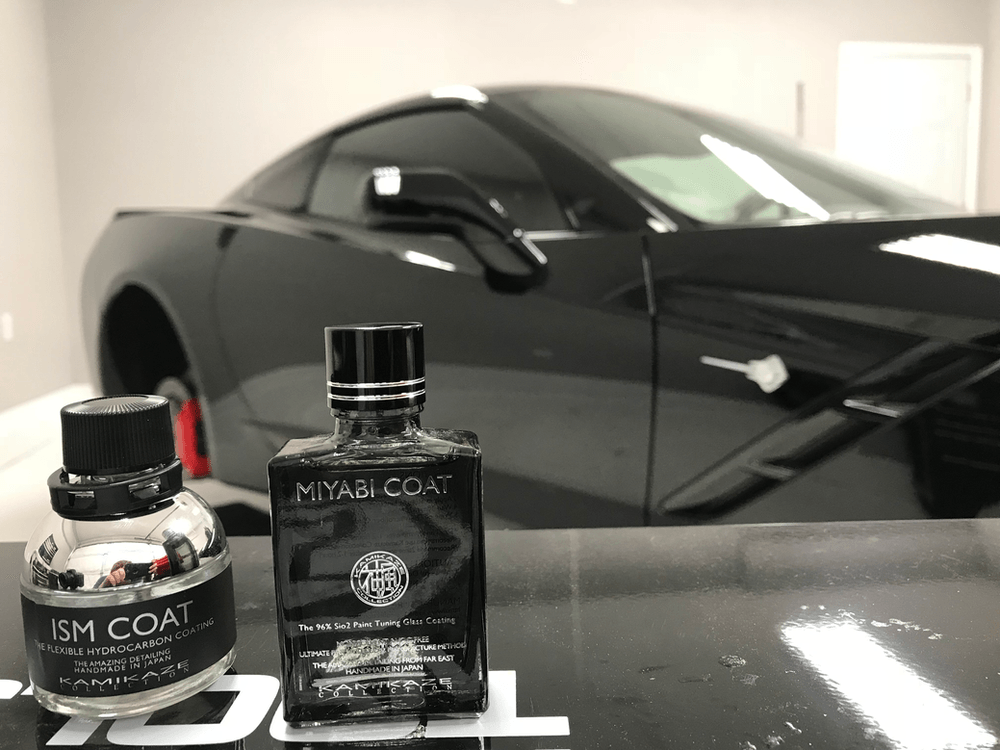Two bottles of ism coat are sitting on a table in front of a black car.
