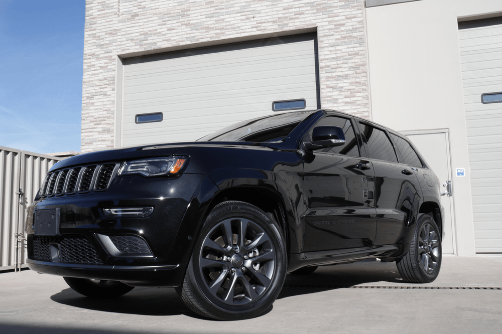 A black jeep grand cherokee is parked in front of a garage door.