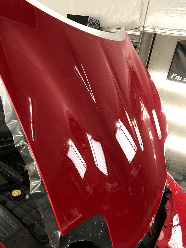 The hood of a red car is open in a garage.