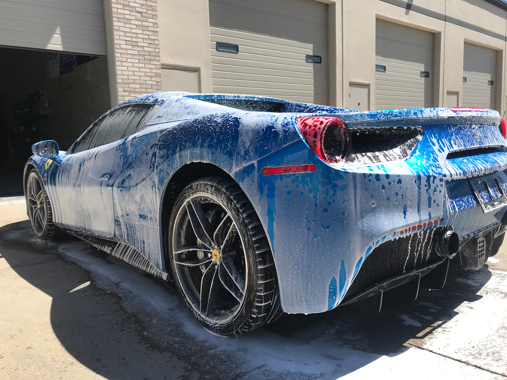 A blue sports car covered in foam is parked in front of a garage.