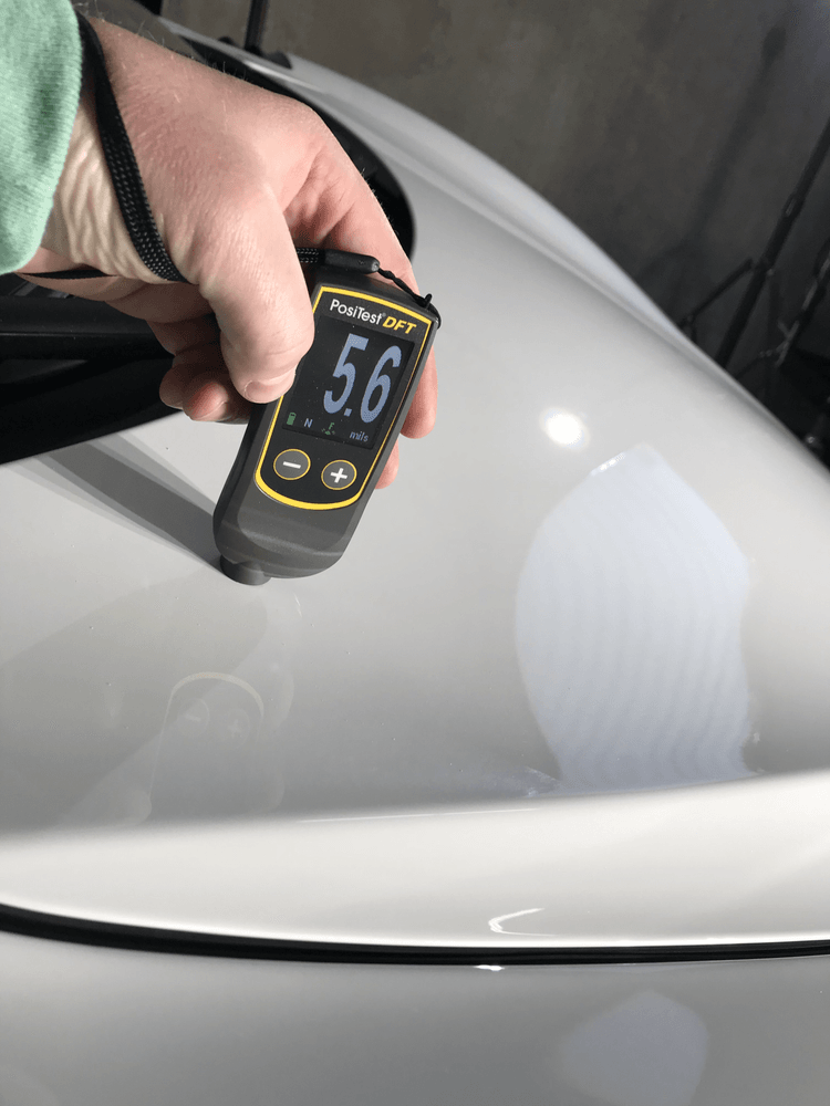 A person is measuring the thickness of a white car